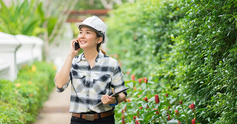 Female landscaper on cell phone and holding tablet on site