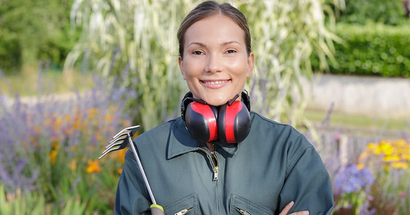 Female landscaper smiling at camera and holding tool