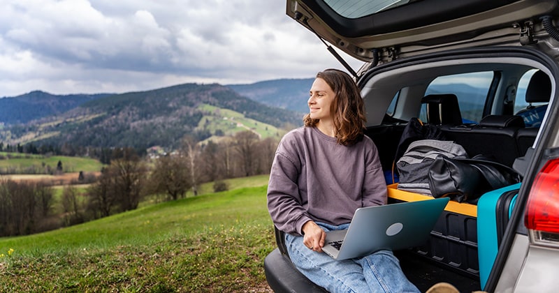 Woman sitting in the trunk of her car practicing landscape design and looking into the mountains